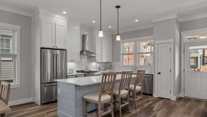 Una cocina moderna con armarios blancos, un refrigerador de acero inoxidable, sillas de madera e iluminación colgante.