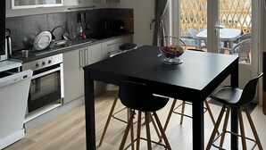 A modern kitchen with white cabinetry, a black dining table, and a view of the outside through large windows. - Appartement Terrasse (Armentières)