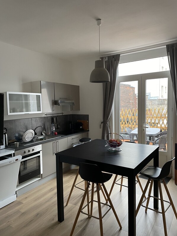 A modern kitchen with white cabinetry, a black dining table, and a view of the outside through large windows.