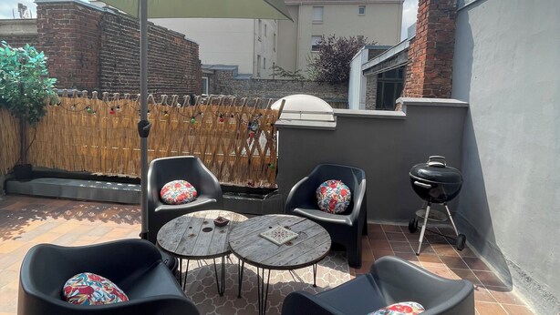 A patio with outdoor furniture, a barbecue grill, and a view of a residential building. - Appartement Terrasse (Armentières)