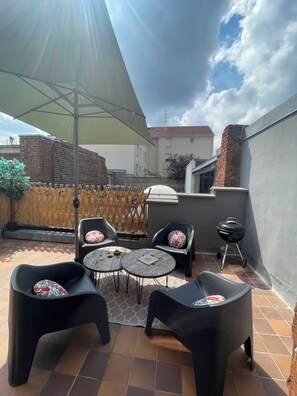 En terrasse med udendørs møbler, grill og udsigt til et boligkompleks.