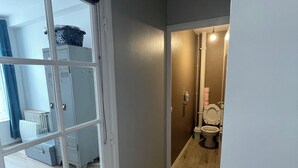 A hallway with a wooden floor leading to a bathroom with a toilet and a sink. - Appartement Terrasse (Armentières)