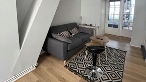 A modern living room with a grey sofa, a patterned rug, and a wooden floor. - Appartement Terrasse (Armentières)