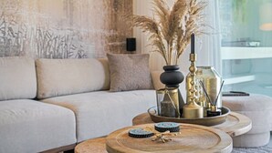 A living room with a sofa, a coffee table with decorative items, and a wall with a textured mural. - Modern Villa with Terrace View, Private Pool & BBQ (Rethymno)