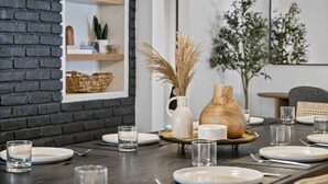 A dining table set with plates, glasses, and a vase with dried plants.