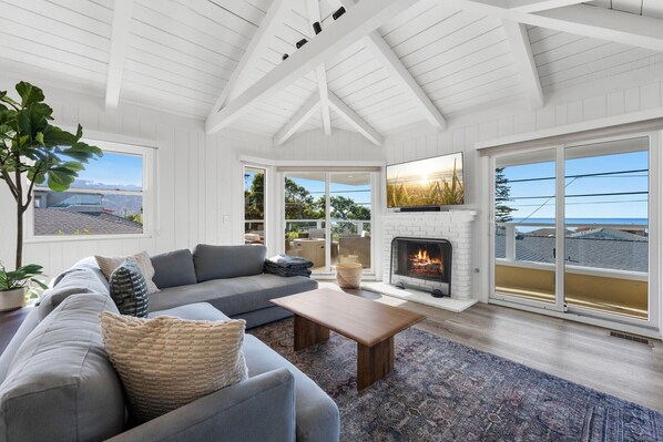 A living room with a fireplace, large windows, and a view of the outdoors. - Tradewinds La Jolla Shores Hot Tub & Ocean Views (San Diego)