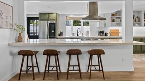 A modern kitchen with a large island, bar stools, and green cabinets.
