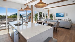 Een moderne keuken met een groot schiereiland, hanglampen en uitzicht op de oceaan.