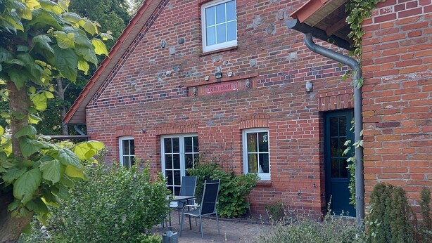 A brick building with a small patio area featuring two chairs and a table. - Vacation at the Uhlenhoff Apartment Bansmeer (Ihlow)
