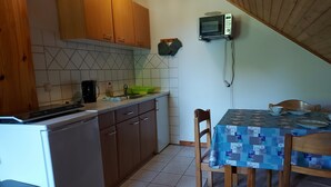 A kitchen with wooden cabinets, a microwave, a coffee maker, and a dining table with chairs. - Vacation at the Uhlenhoff Apartment Bansmeer (Ihlow)