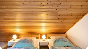 A room with wooden slatted ceiling, two bedside tables with lamps, and two beds with patterned bedding. - Vacation at the Uhlenhoff Apartment Bansmeer (Ihlow)