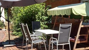 An outdoor patio with a table and chairs, a swing set, and a brick wall. - Vacation at the Uhlenhoff Apartment Bansmeer (Ihlow)