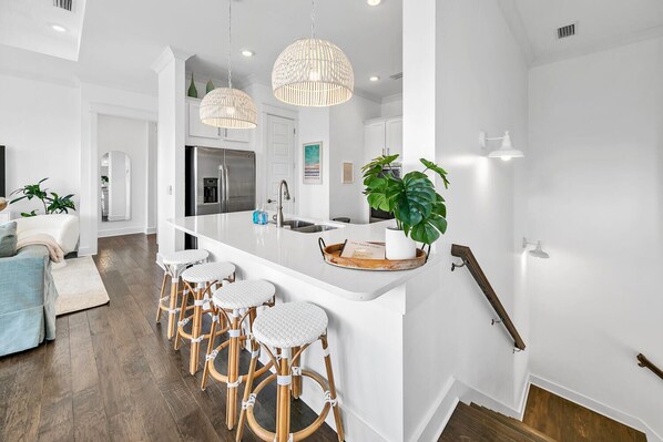 Una cocina moderna con armarios blancos, un refrigerador de acero inoxidable y una isla central con taburetes de bar.