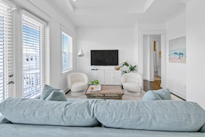 Una sala de estar moderna con un sofá gris, dos sillones, una mesa de centro y un televisor en la pared.