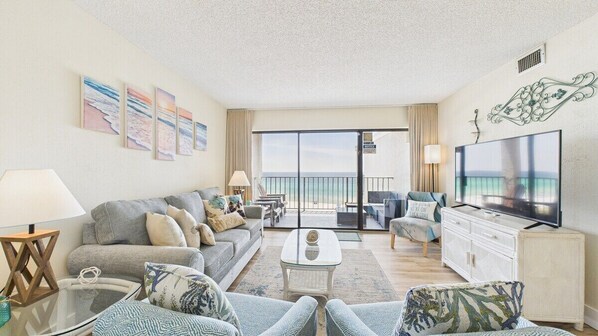 Un salon spacieux comprenant un canapé, des fauteuils, une table basse et un téléviseur. Il y a également un balcon avec vue sur l’océan.