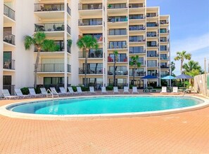 A multi-story hotel with a swimming pool, outdoor seating, and palm trees. - Take Me A Wave 806–Ocean Views–Sleeps 4 (Panama City Beach)