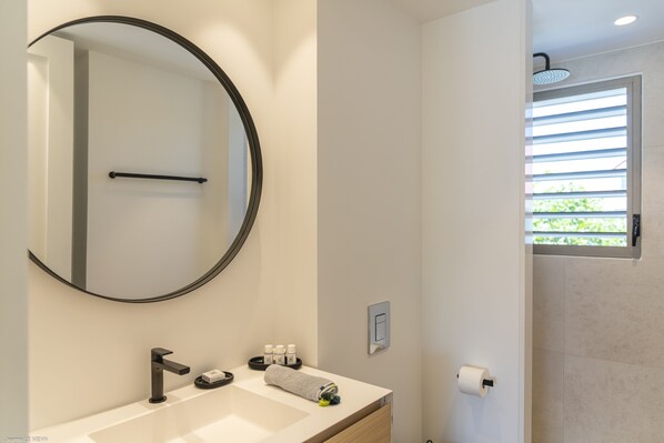 A modern bathroom with a round mirror, a sink, a towel, and a shower area. - Sunshine 7 (Collectivity of Saint Martin)