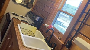 A kitchen with wooden walls, a stove, a sink, and a window with a view of trees. - Log Cabin located on the Greenbrier River in Hinton WV (Hinton)