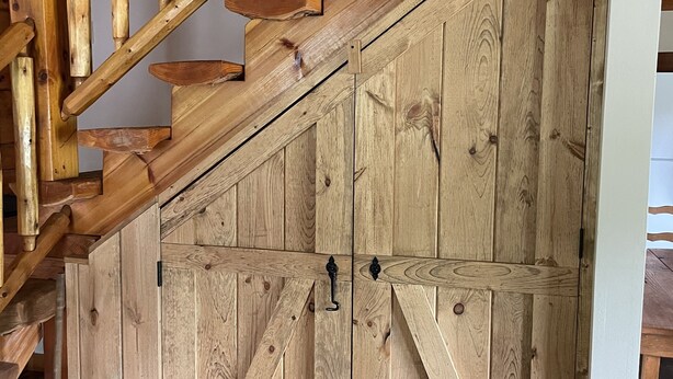 A wooden staircase with a rustic design, leading to a room with a large wooden wardrobe. - Log Cabin located on the Greenbrier River in Hinton WV (Hinton)