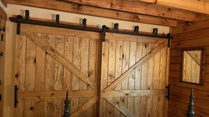 A bedroom with a large wooden wardrobe, a bed with a plaid bedspread, and a small mirror on the wall. - Log Cabin located on the Greenbrier River in Hinton WV (Hinton)