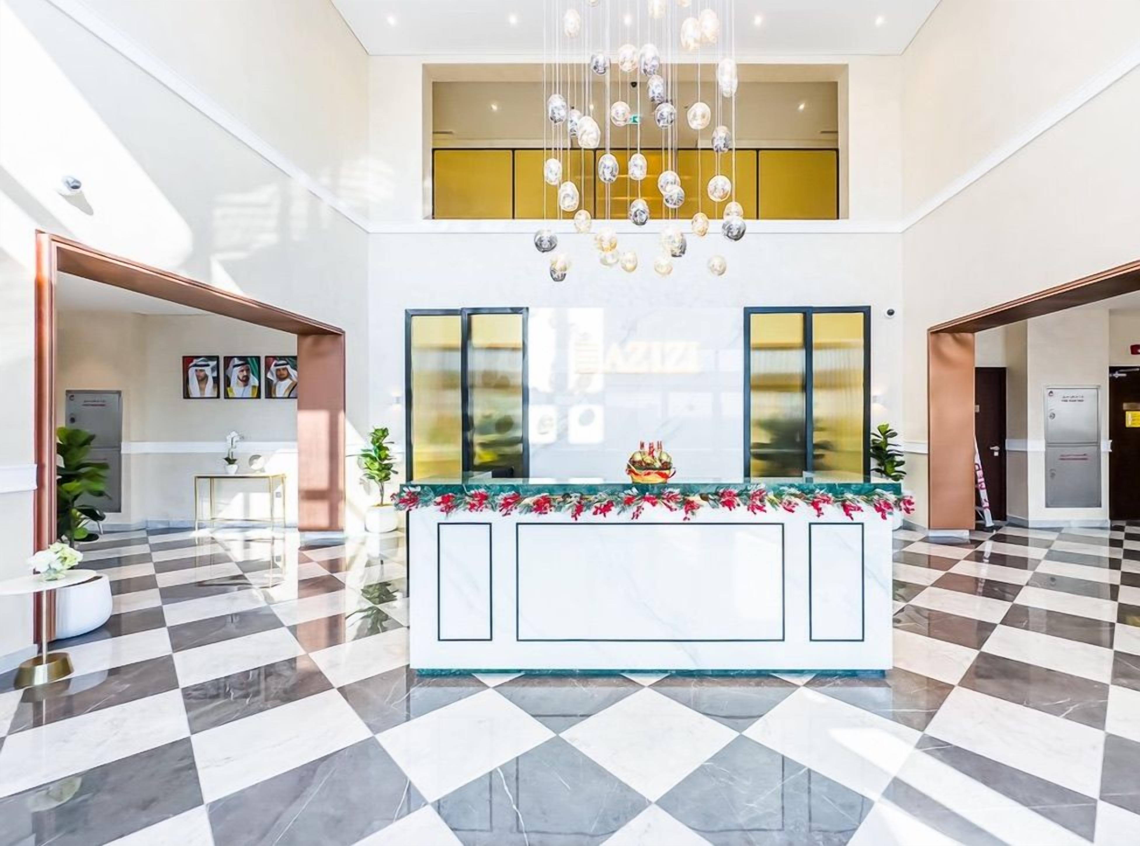 Eine Hotelhalle mit Schachbrettmuster-Boden, einem Empfangstresen mit Blumenarrangement und einem Chandelier.