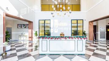 Eine Hotelhalle mit Schachbrettmuster-Boden, einem Empfangstresen mit Blumenarrangement und einem Chandelier.