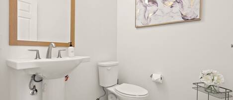 Un baño con un lavabo blanco, un inodoro, un espejo con marco de madera y un cuadro abstracto en la pared.