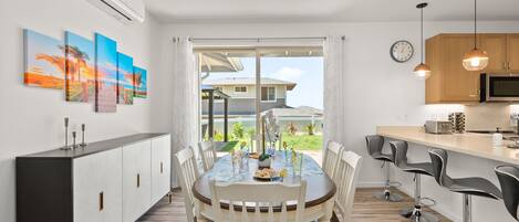 A modern kitchen with a dining area, featuring a large window, a dining table with chairs, and a kitchen counter with bar stools.