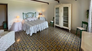 Un dormitorio con piso estampado, una cama con cabecera verde, dos lámparas de noche, un armario blanco y una silla.