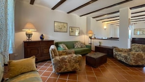 Una sala de estar con un sofá verde, sillones estampados, un aparador de madera y piso de baldosas.