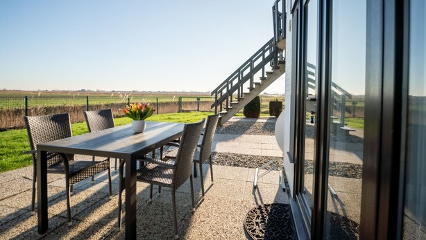 An outdoor patio with a table and chairs, a potted plant, and a view of a rural landscape. - Giuliott with parking and shared pool by Interhome (De Haan)