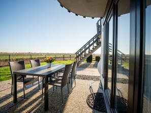 An outdoor patio with a table and chairs, a potted plant, and a view of a rural landscape.