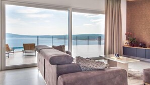 A modern living room with a large sofa, a coffee table, and a view of the sea through floor-to-ceiling windows. - Villa Murn by Interhome (Crikvenica)