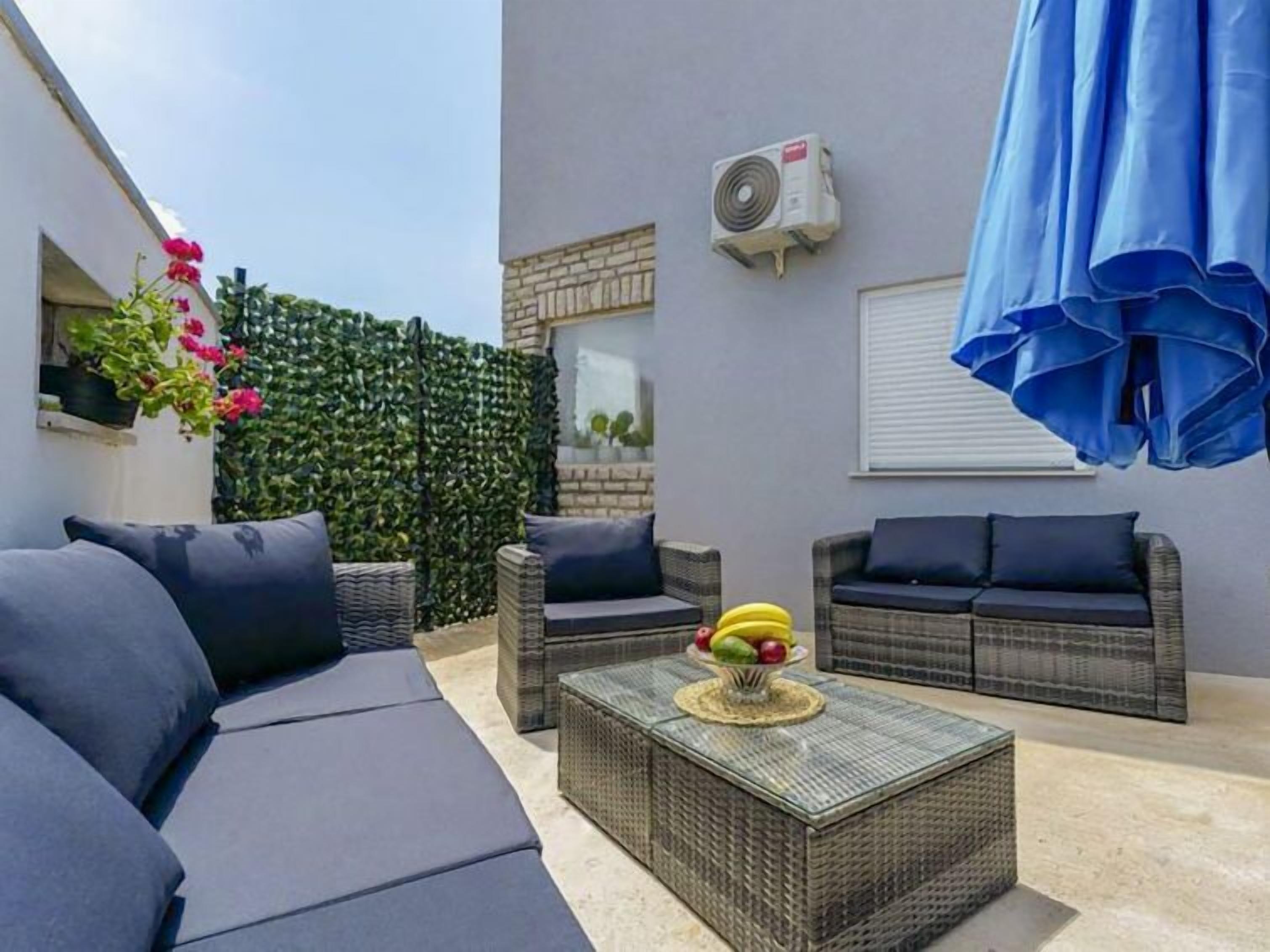A modern outdoor seating area with wicker furniture, a central coffee table with fruit, and an air conditioning unit on the wall.