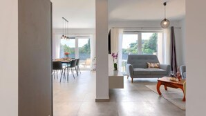 Amplia sala de estar con un sofá gris, una mesa de comedor con sillas y un ventanal con vistas a zonas verdes.