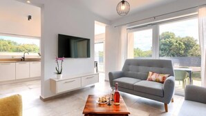 Una sala de estar moderna con un sofá gris, una mesa de centro de madera y un televisor instalado en la pared.