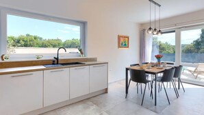 Una cocina moderna con un ventanal grande, un comedor con mesa y sillas, y vista a zonas verdes.