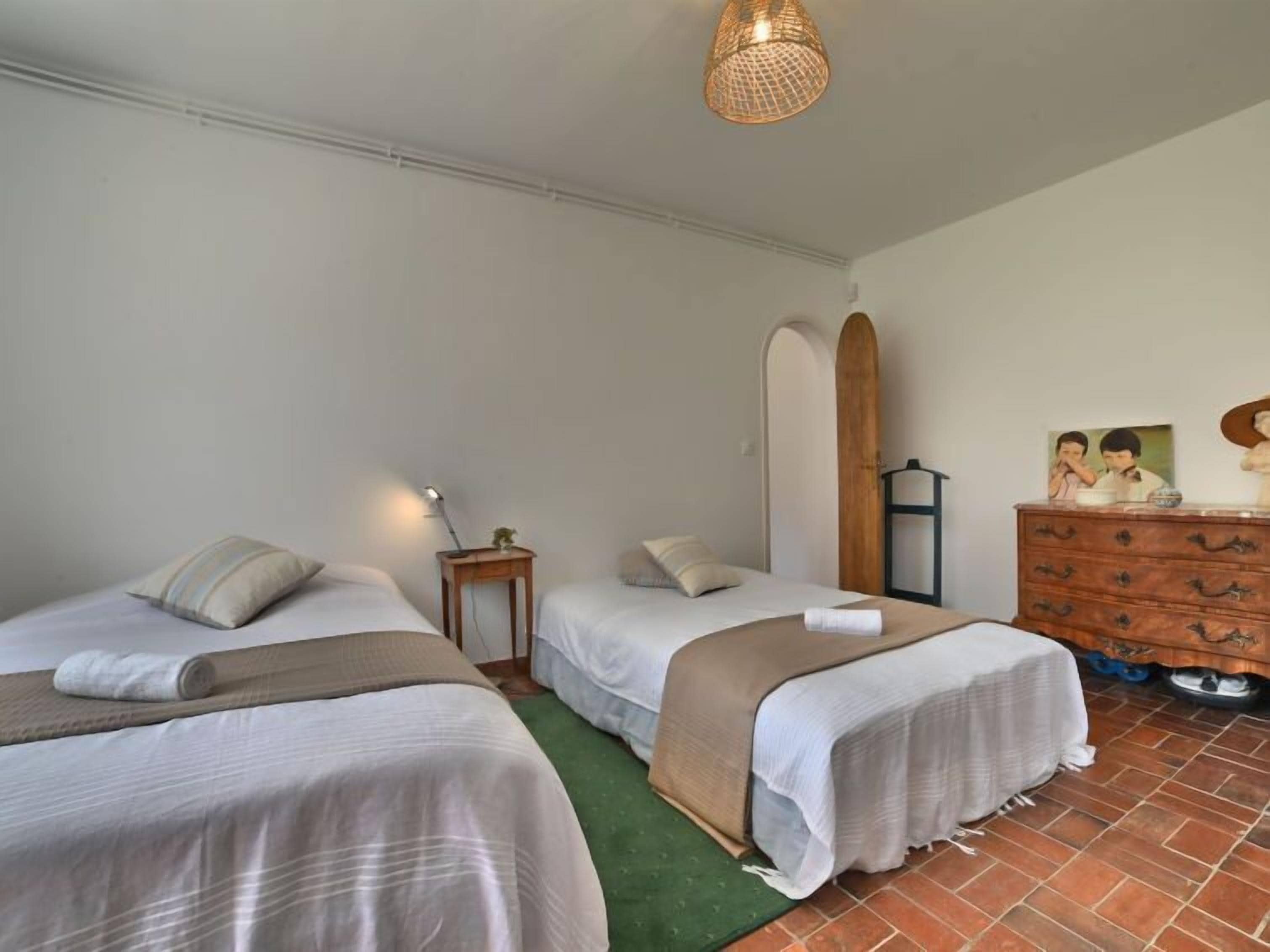 Habitación de hotel con dos camas, un aparador, una tabla de surf y una lámpara.