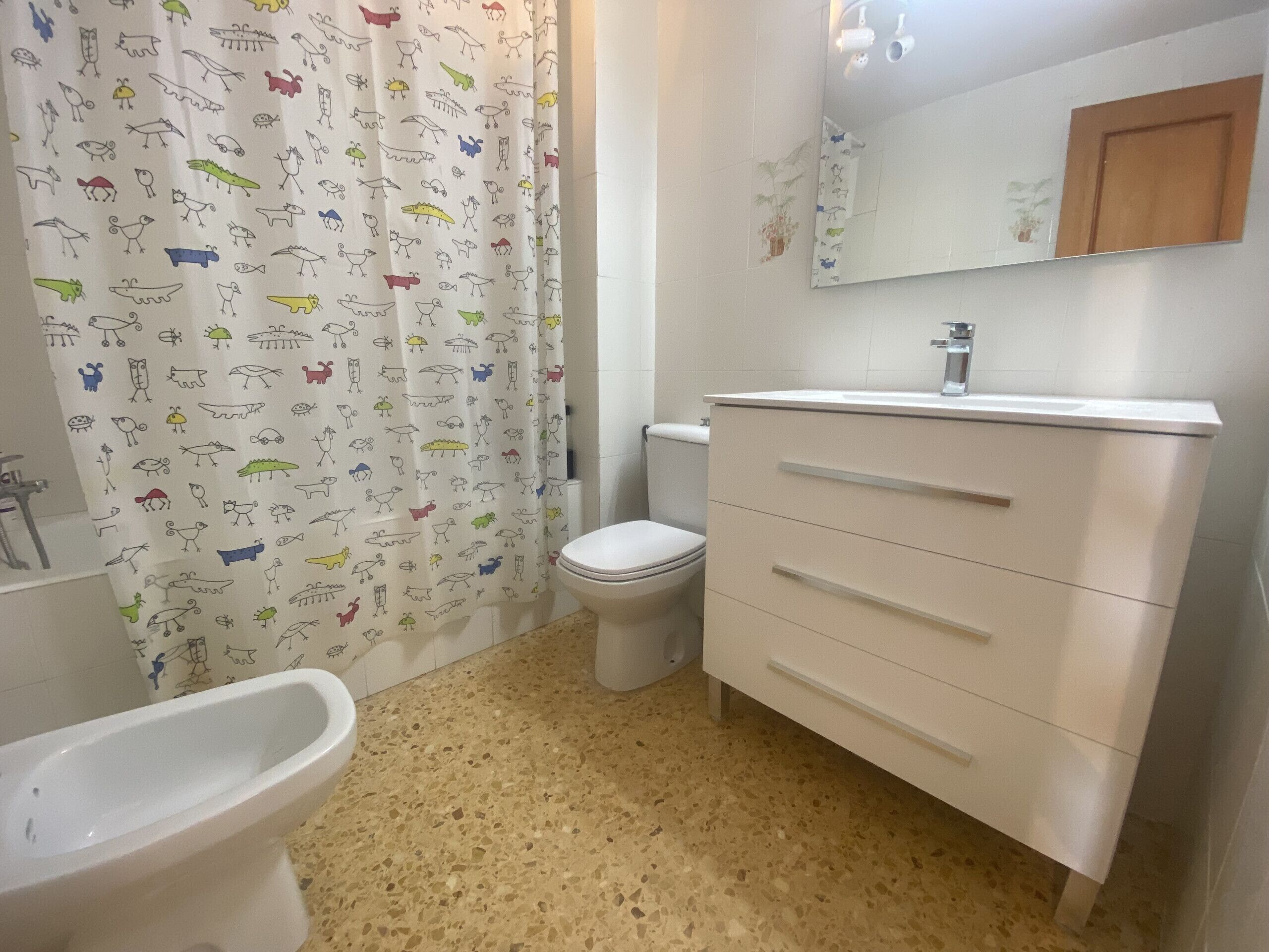 Une salle de bain avec un lavabo blanc, des toilettes, une baignoire et un rideau de douche orné de motifs d’animaux.