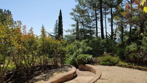 A landscaped garden with a curved concrete pathway, surrounded by various trees and shrubs. - La Tourelle des Ocres by Interhome (Roussillon)