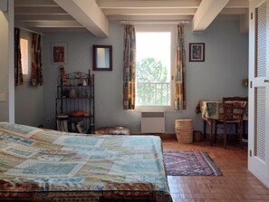 Une chambre à coucher avec un lit, une fenêtre avec des rideaux, un radiateur, une chaise et une petite table.