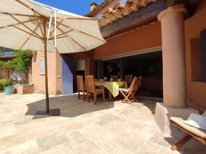 Une terrasse extérieure avec une table et des chaises, un grand parasol et un sol en pierre.
