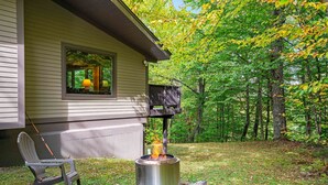 A patio with a metal stove, a chair, and a window overlooking a forest. - Alpine Court Chalet 4 Bedroom Home (Killington)