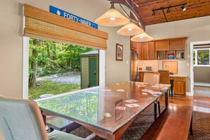 A dining area with a glass table, wooden chairs, and a view of the outdoors.