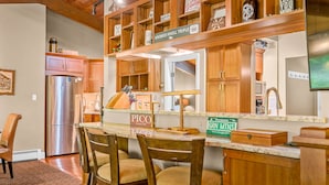 A kitchen with wooden cabinets, a stainless steel refrigerator, a wooden dining table with chairs, and a countertop with a coffee machine. - Alpine Court Chalet 4 Bedroom Home (Killington)
