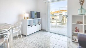 Ein modernes Wohnzimmer mit Fernseher auf einem weißen Schrank, einem Esstisch mit Stühlen und einer Glastür zum Außenbereich.