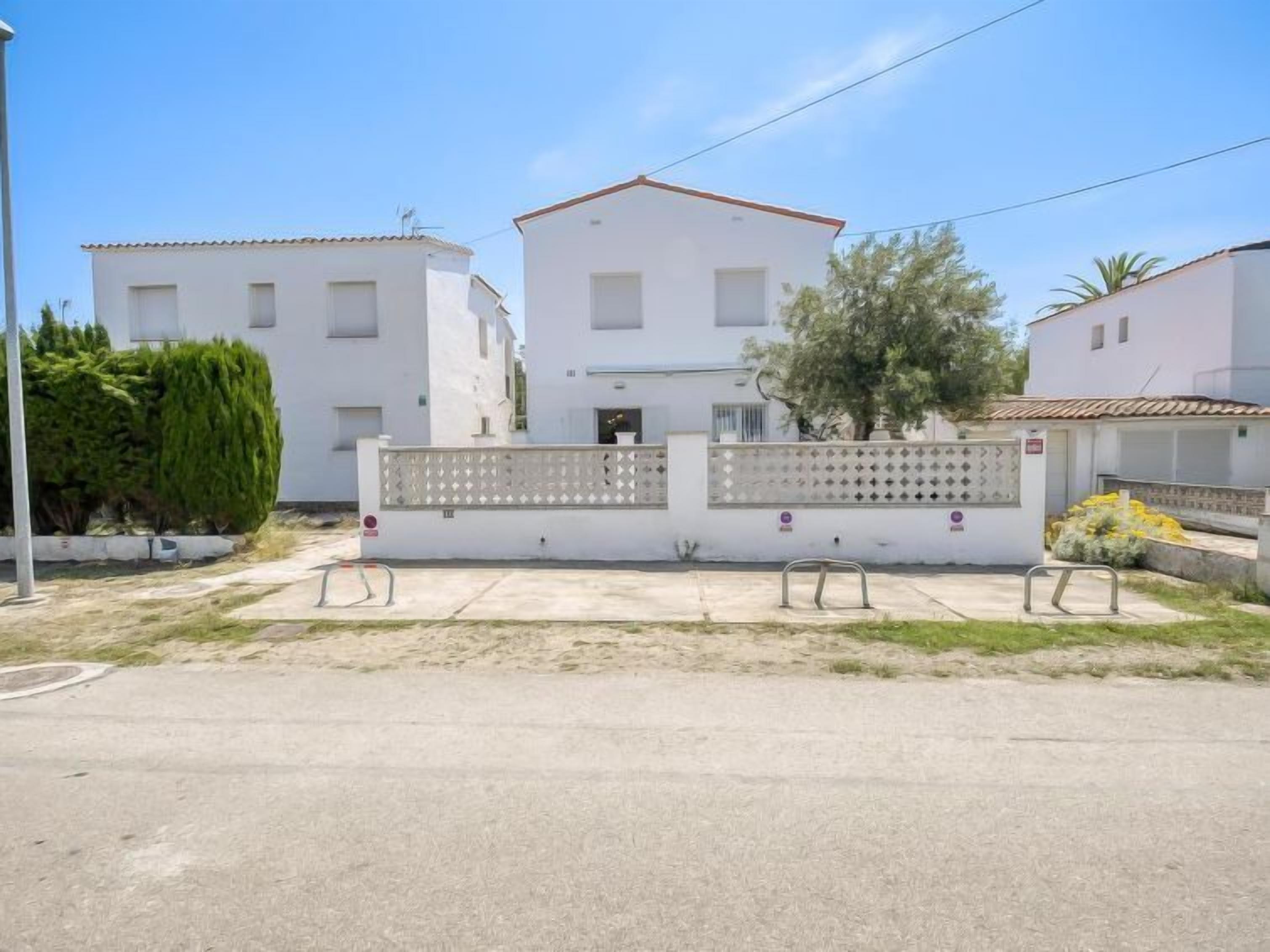 Un bâtiment blanc à deux étages, doté d’un toit en tuiles, d’une entrée fermée par un portail et d’un petit jardin agrémenté d’un arbre et de quelques arbustes.