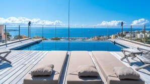 Una piscina infinita con sillones de descanso y vistas despejadas del océano y el paisaje urbano.