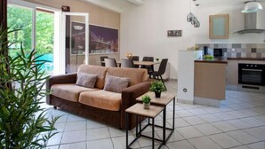 Un soggiorno moderno con divano, un tavolino con piante, un'area pranzo con sedie e una cucina con piano cottura e pensili.