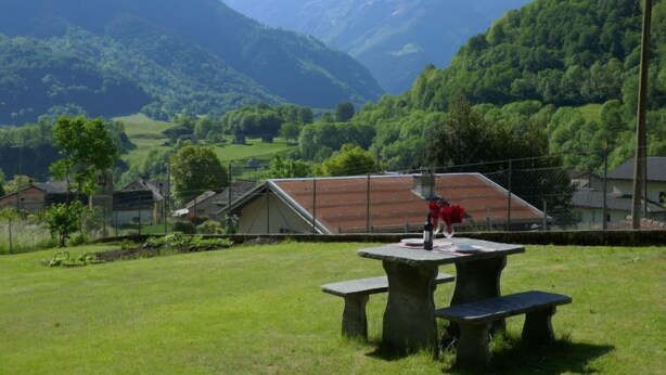 A picnic table with benches in a grassy area with a mountain backdrop. - Apartment Lara by Interhome (Olivone)